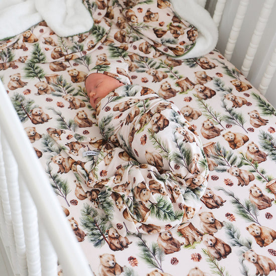 Baby lyig in crib wrapped in nature themed swaddle on matching crib sheet