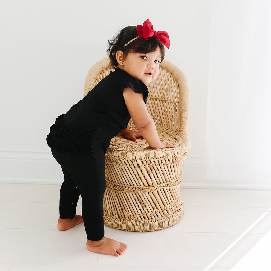 Baby girl leaning on chair in black bamboo baby clothes