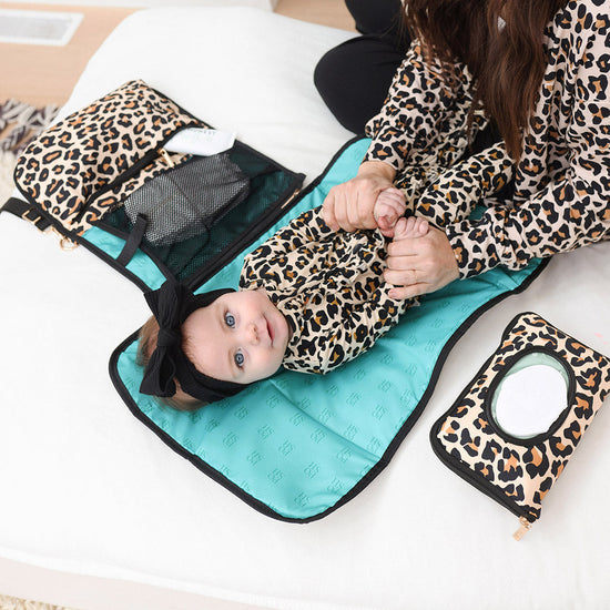 Mother preparing to change baby diaper wearing matching leopard outfits