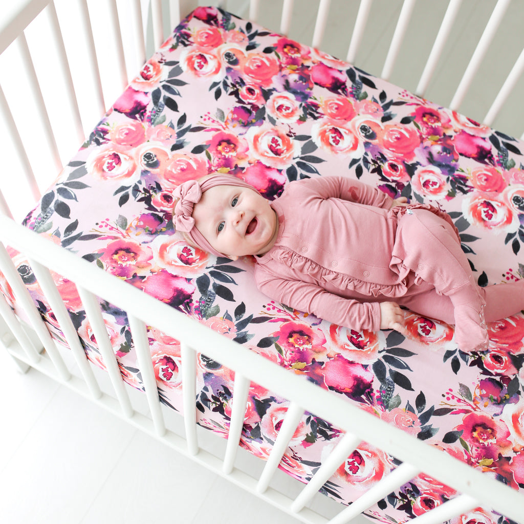 baby girl laying on floral baby crib sheets