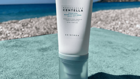 Bild av SKIN1004 - Madagascar Centella Hyalu-Cica Water-Fit Sun Serum, elegant placerad på en handduk med havet som bakgrund. Produkten ger intrycket av effektivt solskydd med en fräsch och naturlig känsla.