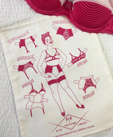 large white canvas storage back printed with an illustration of a woman with vintage hairstlye wearing a 1950s inspired bullet bra, high waisted knickers and seamed stockings. The bag has a drawstring at the top and is perfect for lingerie and seamed stocking storage