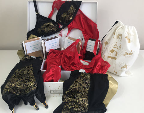 lingerie advent calendar. A large white box with 12 compartments and a piece of handmade vintage inspired lingerie in each. Four compartments include pairs of seamed stockings, gift wrapped in gold tissue paper. The other compartments incluse a set of red satin underwear and an exclusive black and gold lace lingerie set including our favourite 6 strap girdlette and front fastening bralette. The perfect Christmas gift for vintage lingerie lovers