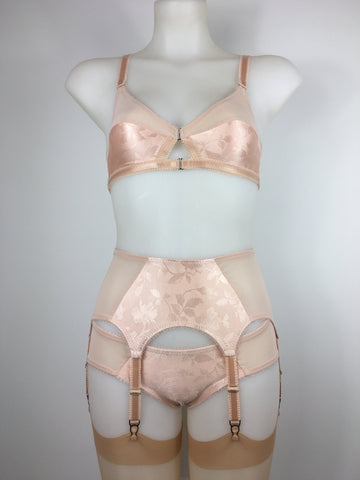 faux vintage inspired longline girdle and front fastening bralette in peachy floral satin fabric. Longline girdle has 6 beige suspender clips holding up seamed nylon stockings. Matching garter belt, longline underwired bra and pantie girdle 