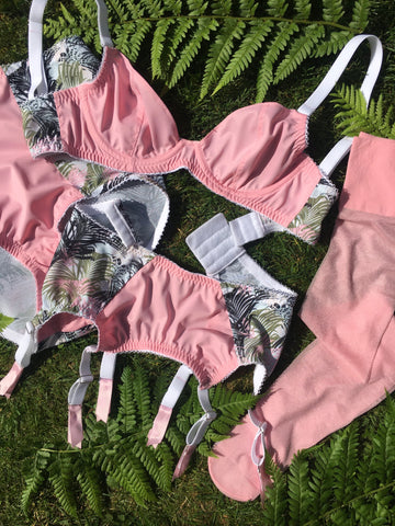 Barbie pink vintage inspired underwear made in the UK, featuring pink plunge bra, six strap suspender belt with metal garter grips and high waisted panties knickers. Retro barbie style underwear in pale pink with a palm leaf print and matching pale pink coloured stockings