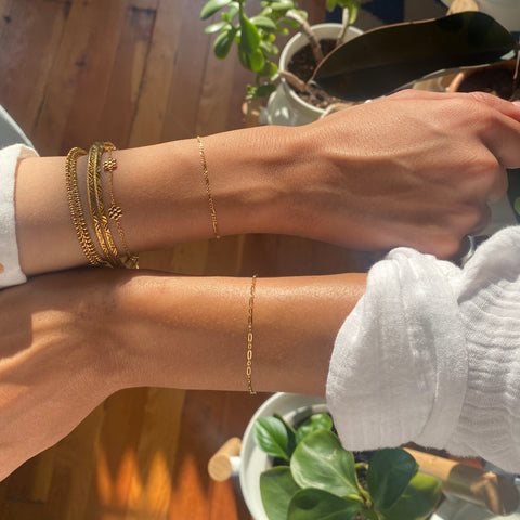 two wrists each are wearing a gold permanent bracelet