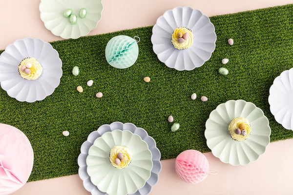 artificial grass runner on a pink table with Meri Meri bamboo scalloped party plates in lavender, green and pink with chocolate easter mini eggs scattered around the plates.