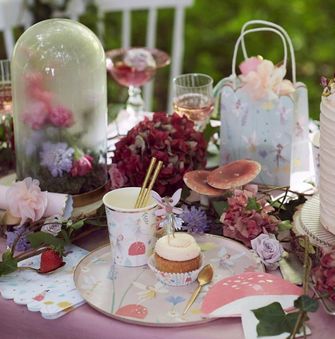 Meri Meri fairy party plate, toadstool napkin, cup and party loot bag set together on a table with flowers and toadstool decorations.