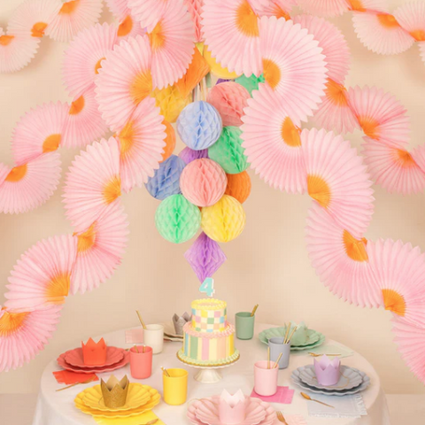 pink tissue paper fans are hanging from the ceiling above a party table set with pastel plates and cups