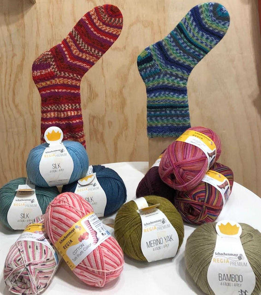 Selection of Regia Sock Yarn in front of 2 hand knitted socks, one red and one blue