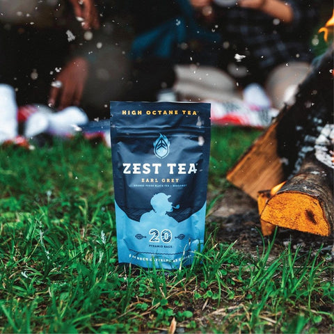 Pouch of Zest Tea Earl Grey standing up on grass at a camp site, with some snow flakes in the air.