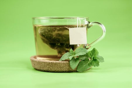 green tea bag steeping in a glass teacup