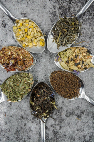 Colorful display of 7 spoons, each containing various types of tea blends