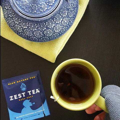 Cup of tea with tea bag still inside, and a Zest Tea Earl Grey opened wrapper displayed next to it.