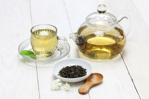 Loose leaf tea with jasmine flowers in front of a tea pot and tea cup