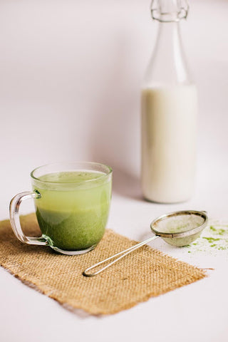 Glass mug with matcha tea, placed next to the sieve that was used to make it