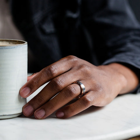 mans hand next to coffee cup on table with ring