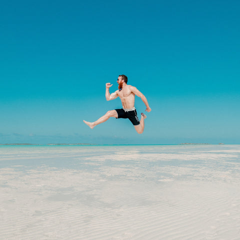 man on beach jumping in water