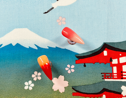Two orange and pink ombre nail tips against a blue sky fabric of a Japanese woodblock print.