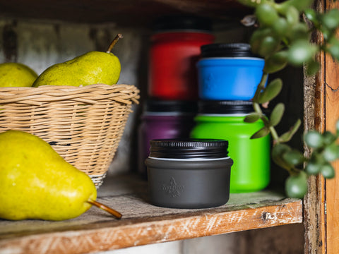 Evergreen stash jars in assorted sizes and colors on a shelf next to a basket of pears