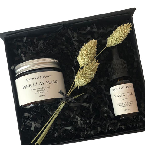 A glass jar of face mask powder and a bottle of face oil in a gift box