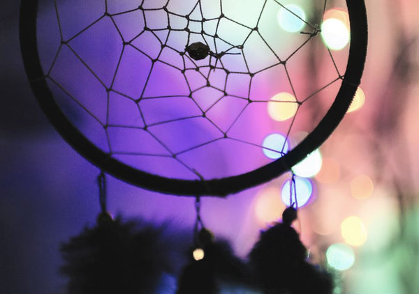 A dreamcatcher with multi-coloured lights in the background