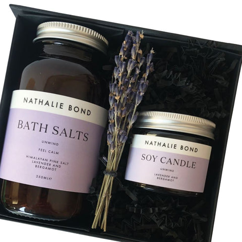 Two glass jars containing bath salts and a soy candle, presented in a black gift box