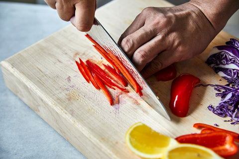 Chef's hand cutting red peppers on a light wooden board