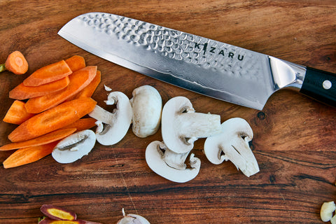 Santoku Kanji knife cutting mushrooms on a dark wooden cutting board