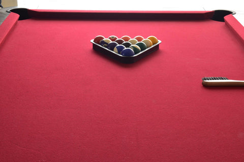 Billiard balls in a black ball rack on a red top pool table with brush.