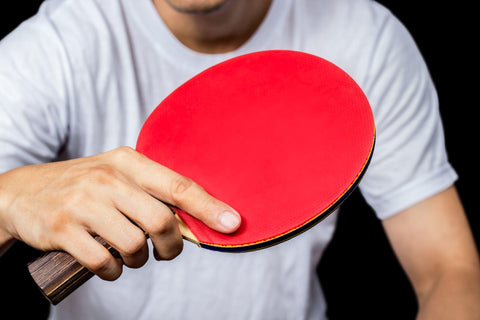 Close up of man holding red ping pong paddle.