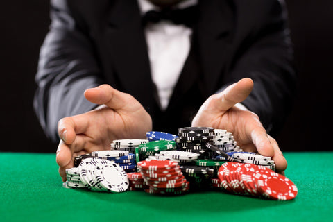 Dealer pushing lots of poker chips on a green poker table.