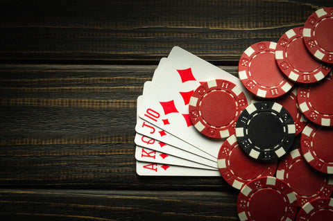 Five poker cards on a wooden table with red and black poker chips.