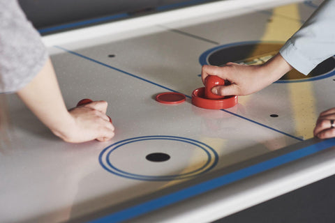 Hands of young people holding striker on air hockey table
