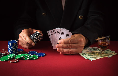 Man holding five poker cards with his left hand and poker chips in his right hand with money on a red poker table.