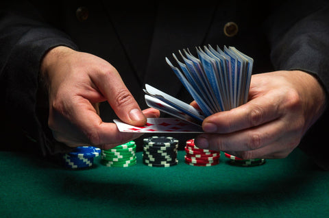 Man shuffling poker cards on a green poker table with poker chips.