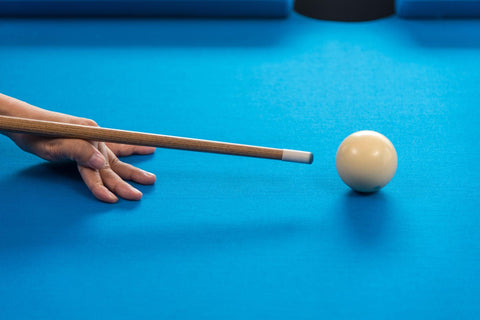 Person hitting white ball on billiard table.