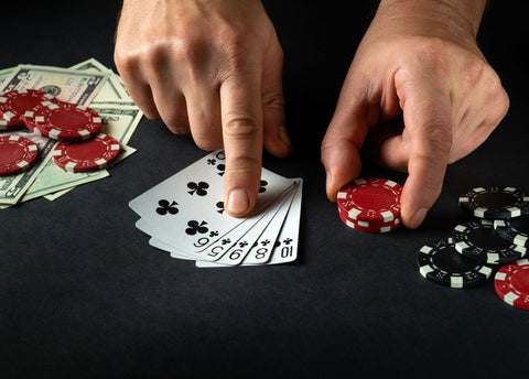 Person pointing to five poker cards on a black poker table with money and chips on table. 