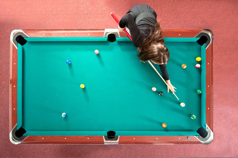 Pool table from above with woman aiming and shooting.