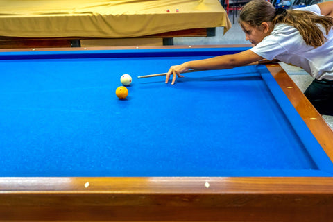 Teenage girl aiming at a ball on carom billiards table.