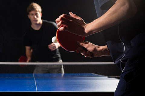 Two ping pong players playing ping pong on blue table.