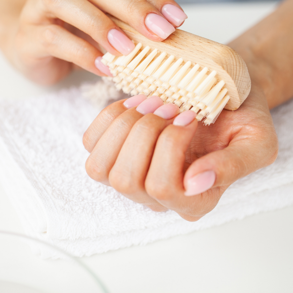 women's hand using nail brush to clean nails