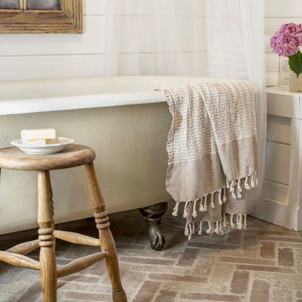 beige clawfoot tub with linen towel draped over the side and wooden stool 