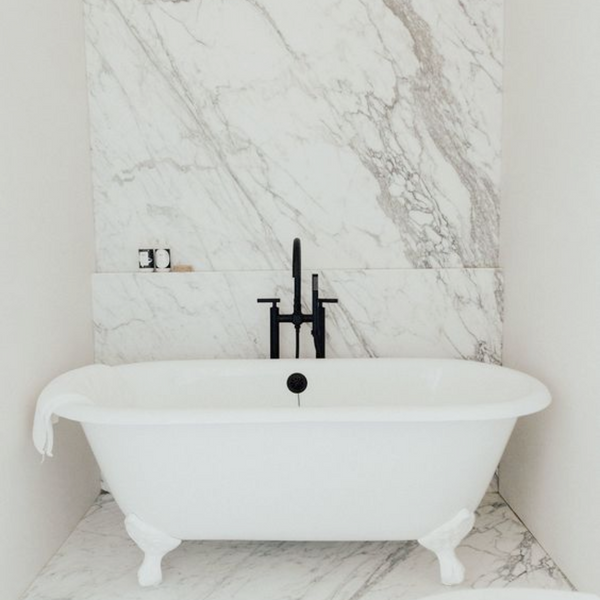 white clawfoot tub with white and grey marble wall behind