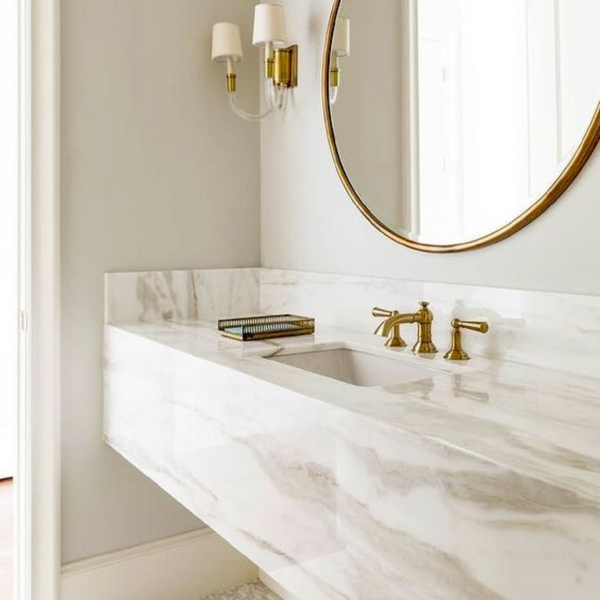 natural marble vanity with beige veining with round gold mirror above and wall scone lighting