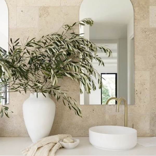 large plant in white vase beside bathroom sink with arched mirror above