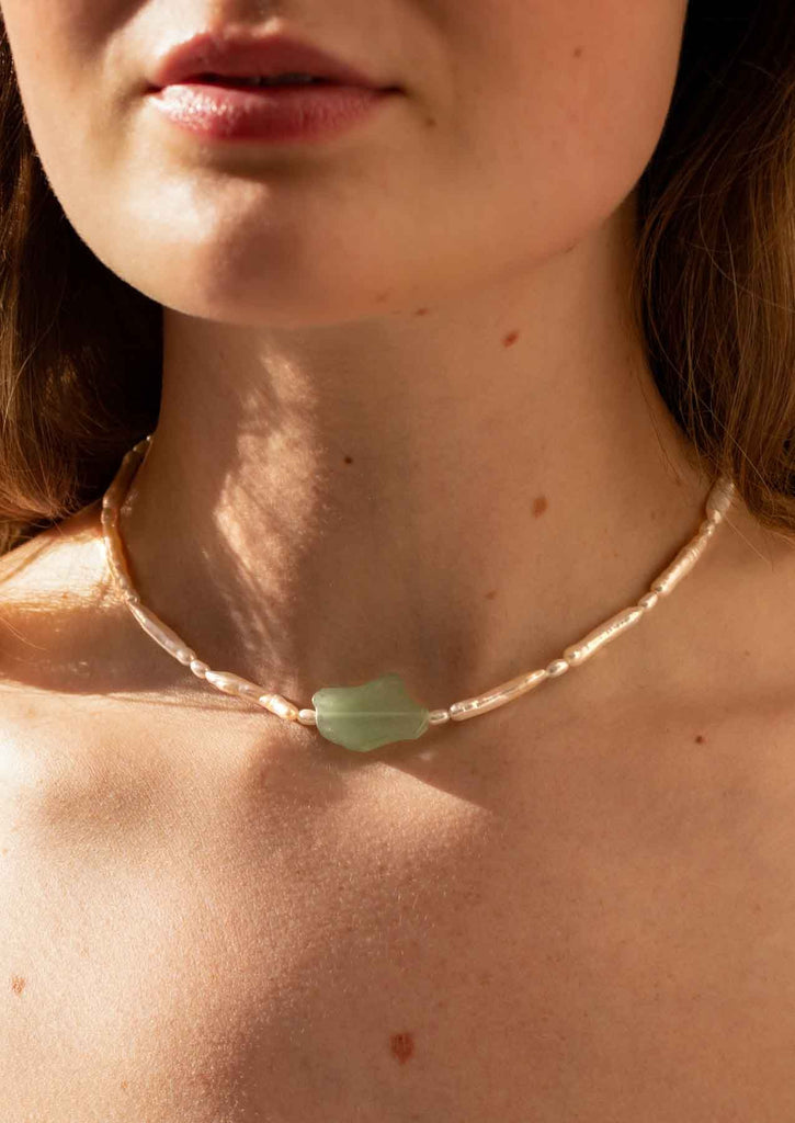 Close up image of a woman wearing a pearl and aventurine necklace.