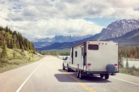 A truck pulling a travel trailer away down a scenic road