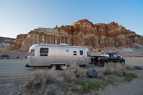 Truck pulling an aluminum AirStream style trailer parked next to a desert cliff side