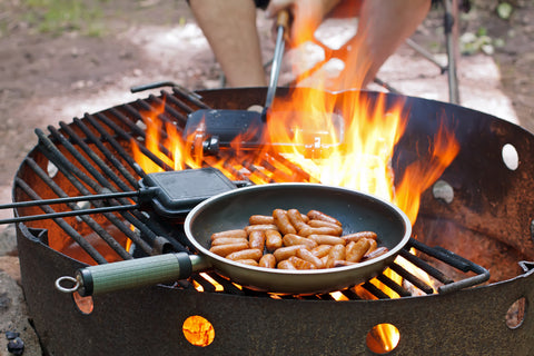 A frying pan and a cast iron pie cooker over a campfire